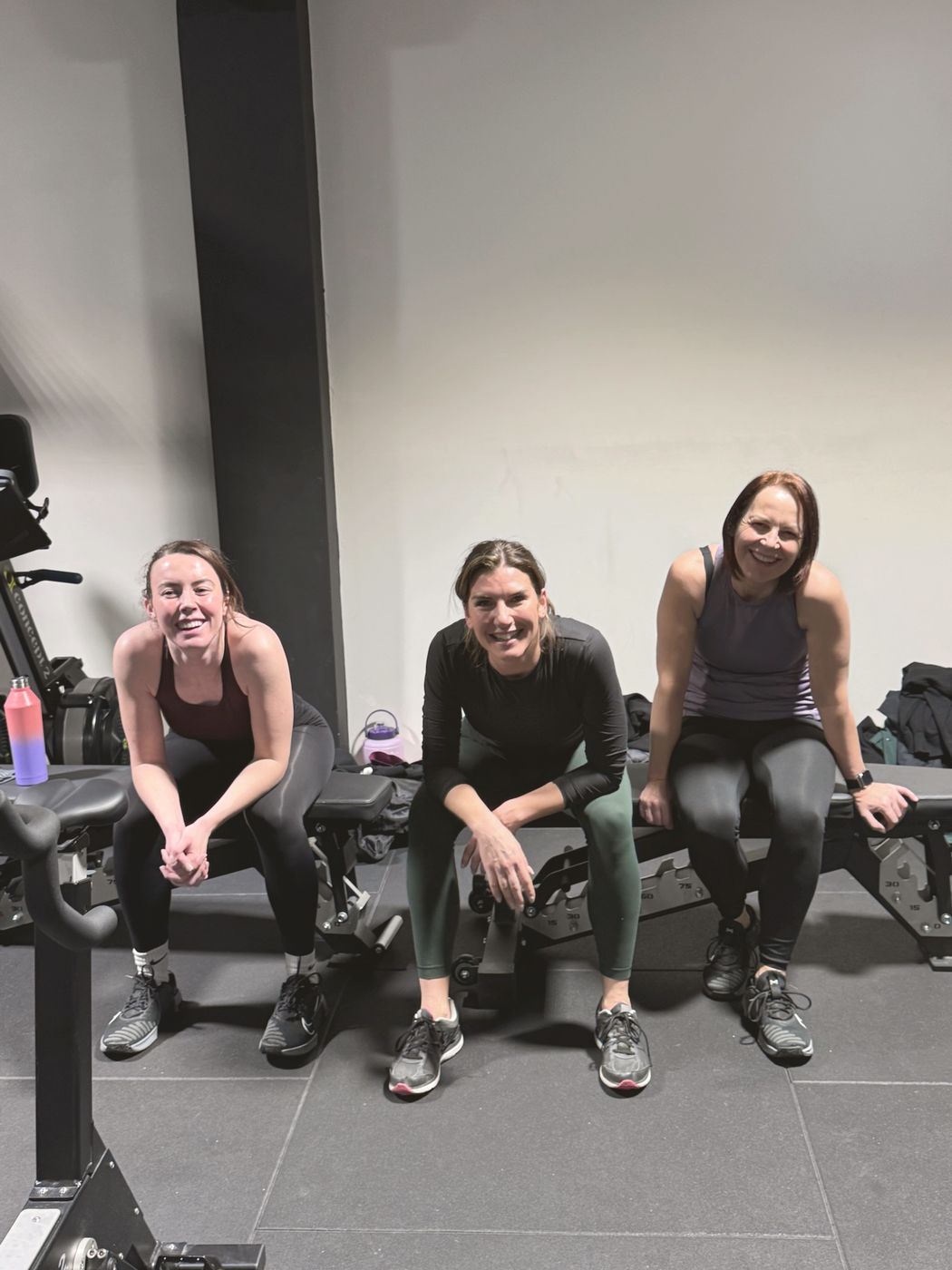 Three members sitting on a bench in the studio, chatting and smiling