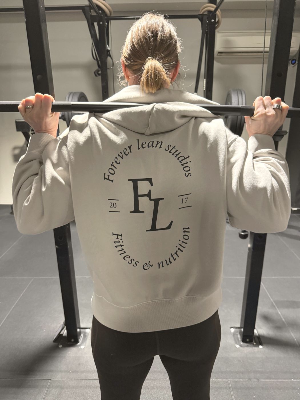 A member in a Forever Lean Studios hoodie setting up under a barbell